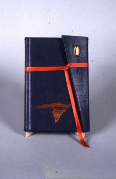 My first commission. Blue leather bound in wallet style. On cover an agate and a hand carved walnut duck. Under the cover a line gilded with variegated copper foil.